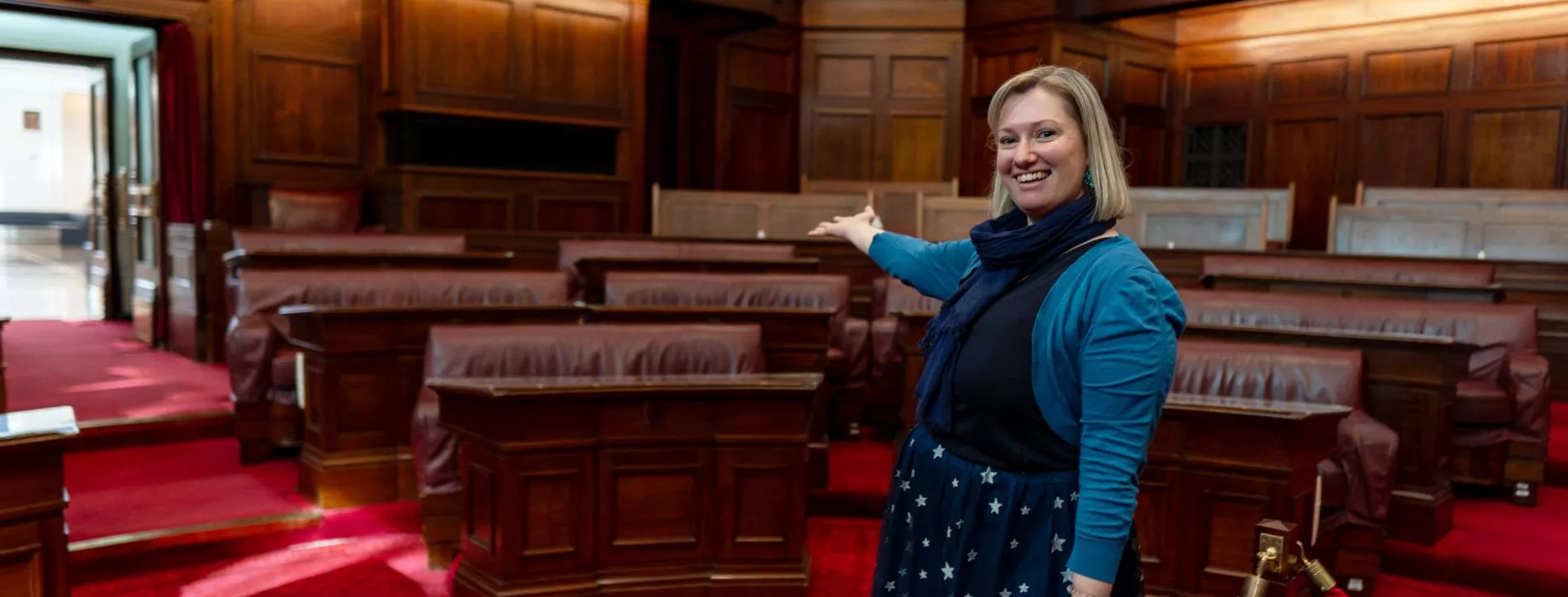 A person stands with their arm outstreched in the senate chamber at old parliament house