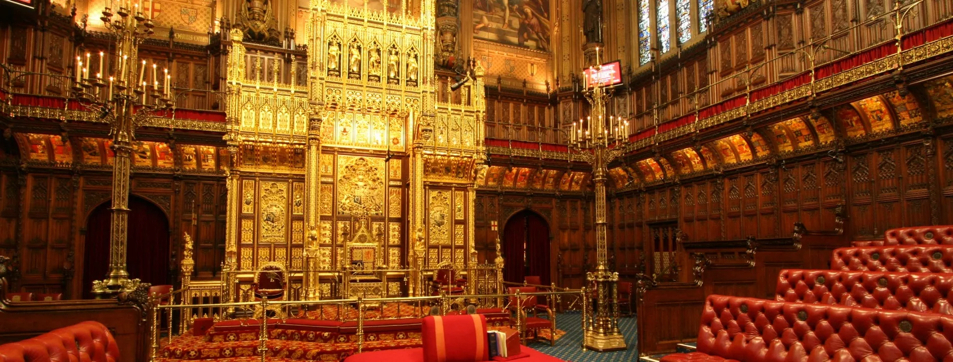 The House of Lords at Westminster, with a golden throne, red leather benches on each side, and big red cushions in the middle.