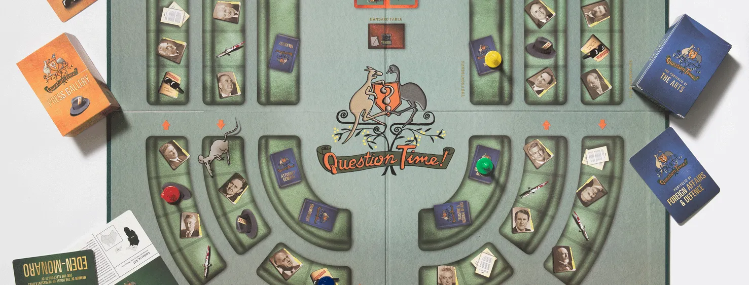 A green board game board opened up showing seats in a horseshoe shape representing the House of Representatives. There are images of politicians on the seats and some game pieces are on top of the board including a blue card with the words Foreign Affairs and Defence and an orange card with the words Stuff ups and scandals. 