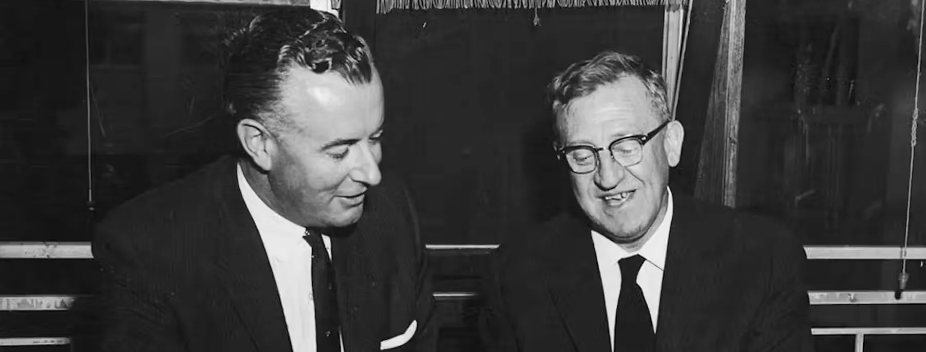 Gough Whitlam and Arthur Calwell sit next to each other, smiling, looking through paper documents together.