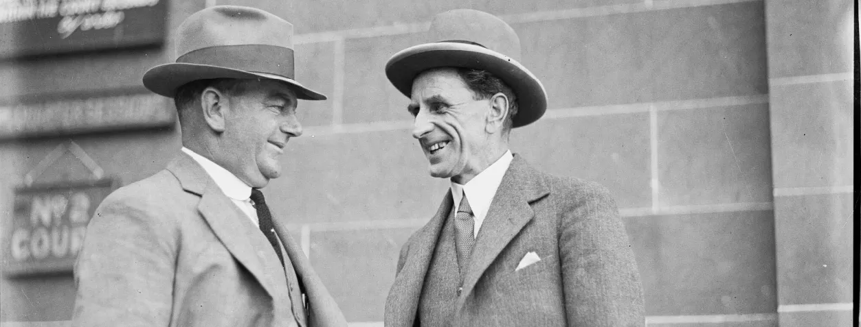 Donald Grant (on the right) smiling and speaking with another man, both wearing wide-brimmed hats and three-piece suits.
