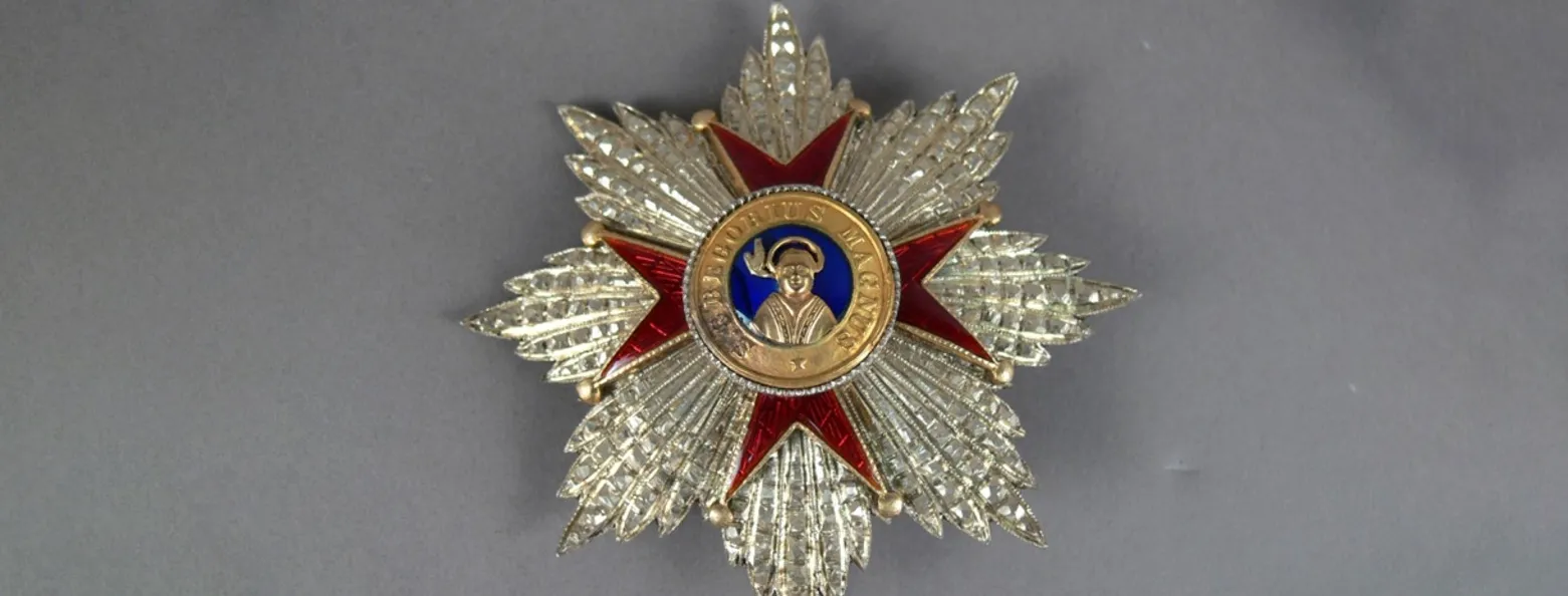 Close-up of a medal in the shape of an ornate silver star, a red cross with a gold centre and the words S. Gregorius Magnus and a golden figure.