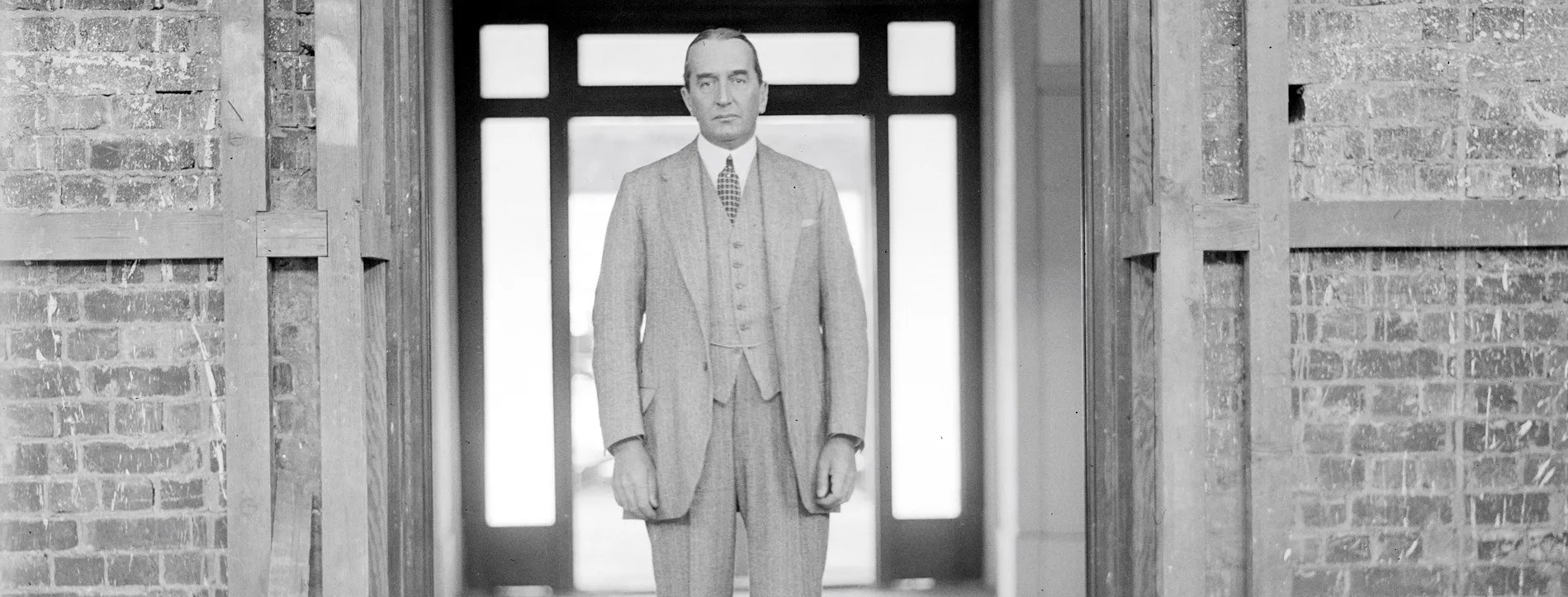 Black and white photograph of Stanley Bruce, wearing a three-piece suit, standing in a doorway at the construction site of Old Parliament House.