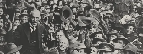 Prime Minister Hughes being held up by a crowd of returning soldiers in a busy street.