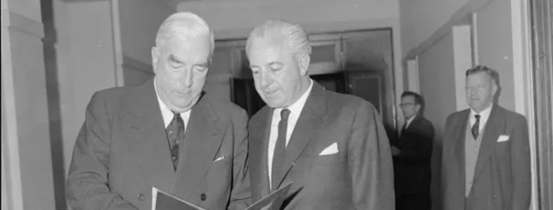 Prime Minister Menzies is holding a document, which both he and Harold Holt are looking at.