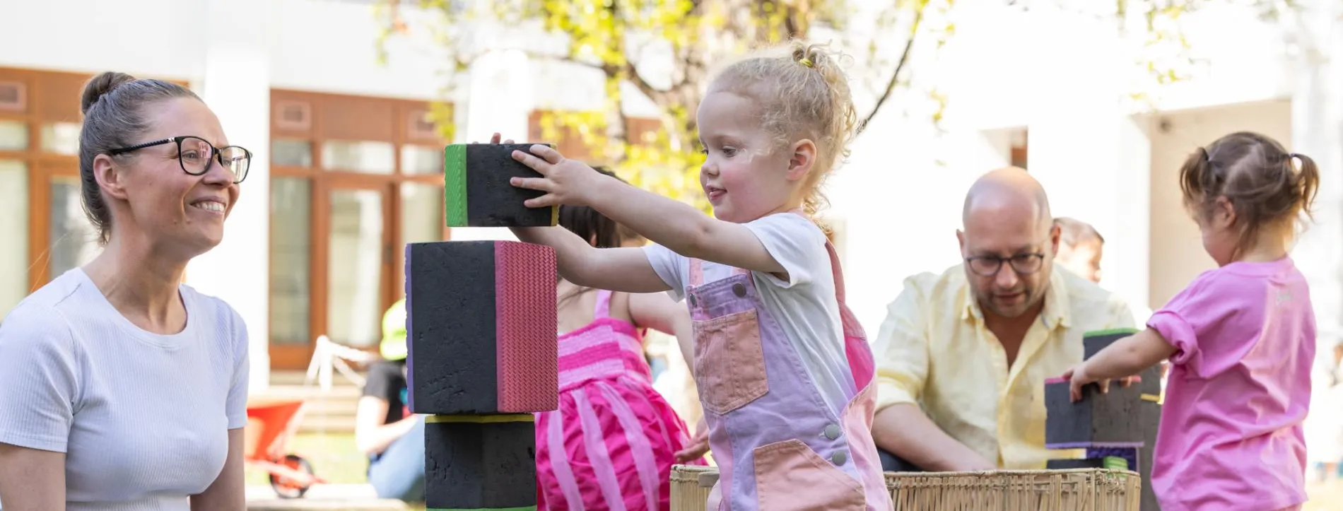 Kids and their parents play with large colourful blocks on the grass of the Old Parliament House courtyard.