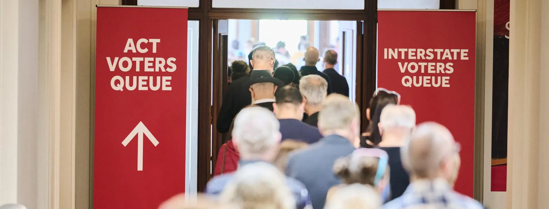 Two red banners, one directing ACT voters and one for interstate voters stand on either side of a doorway filled with people in Old Parliament House.