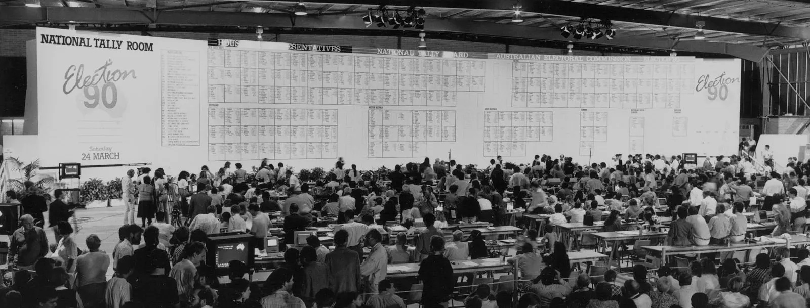 A crowd of people stand in the National Tally Room in Canberra looking at the giant National Tally Room board showing the results of the 1990 election.