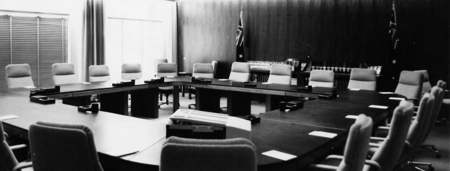The Cabinet Room at Old Parliament House with a square table surrounded by chairs. Two Australian flags stand along a wood panelled wall.