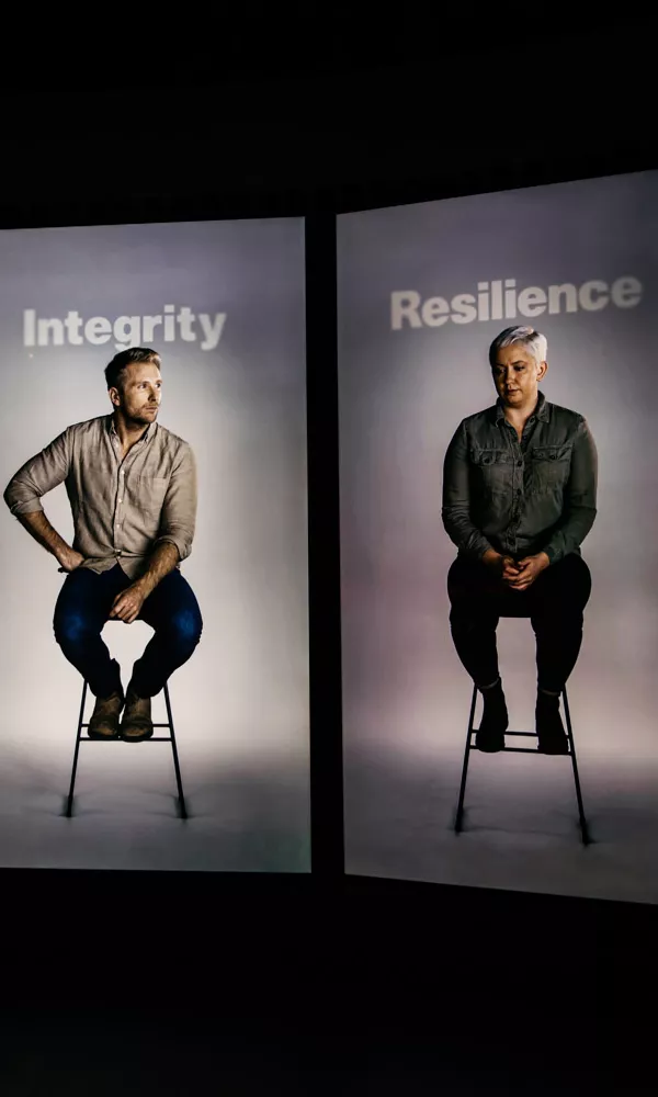 Four video screens with a person sitting on a stool on each screen. The words integrity, resilience and duty appear above them. 