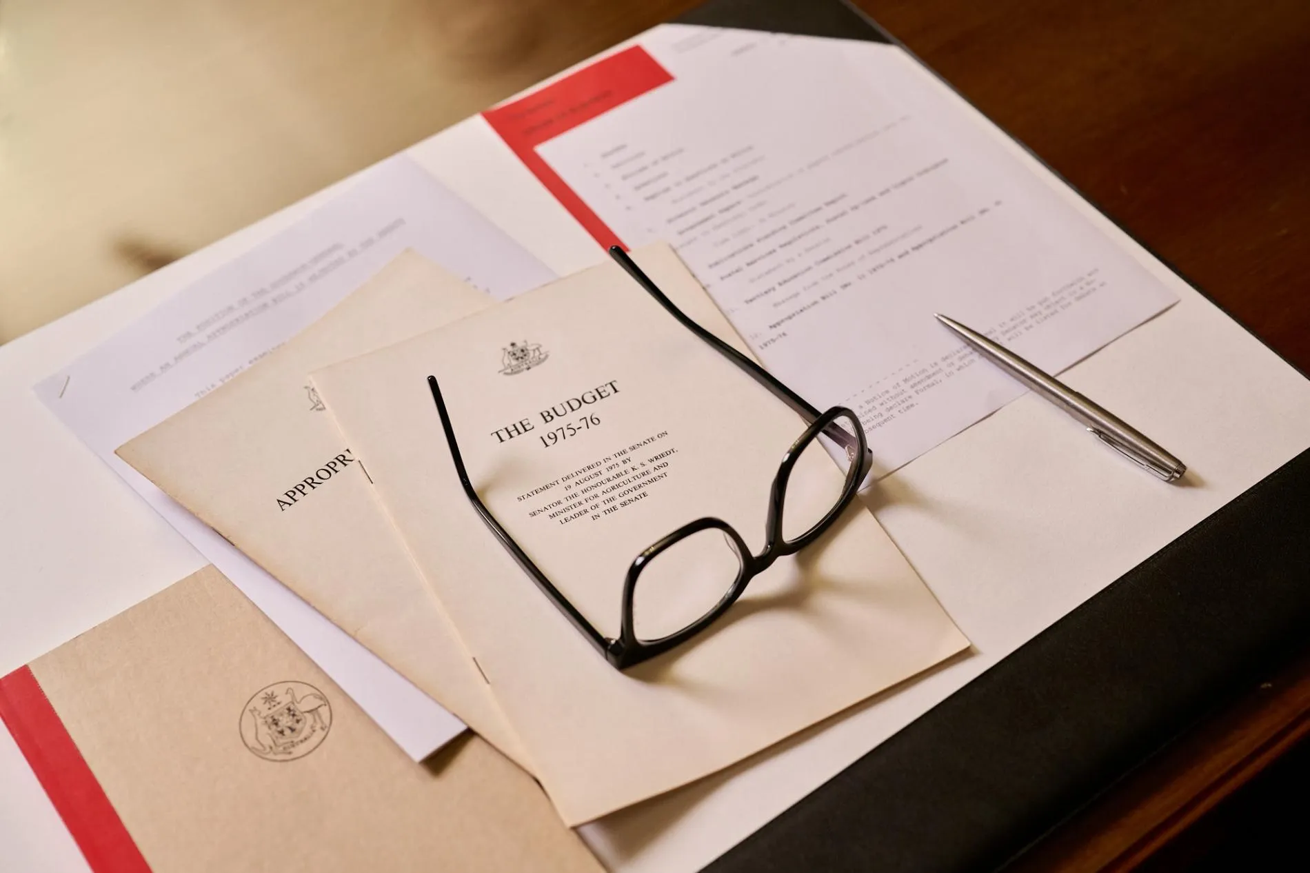 A pair of glasses rest of documents including one titled, 'The Budget 1975-76'.