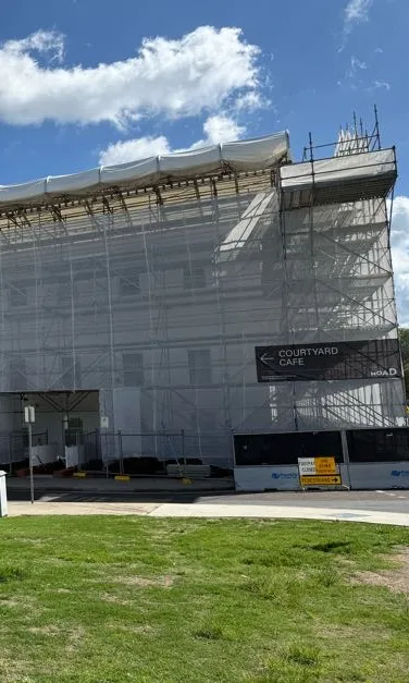 White scaffolding covers the corner of Old Parliament House over 3 levels to the roof which is covered in an awning. A sign reads 'Courtyard Cafe' in large text with an arrow pointing to a doorway.