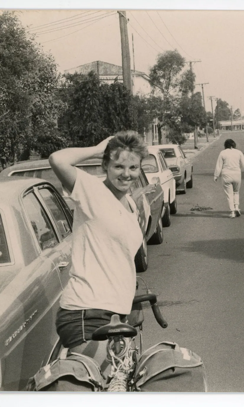 Two women stand with their bicycles beside a car on a suburban street.