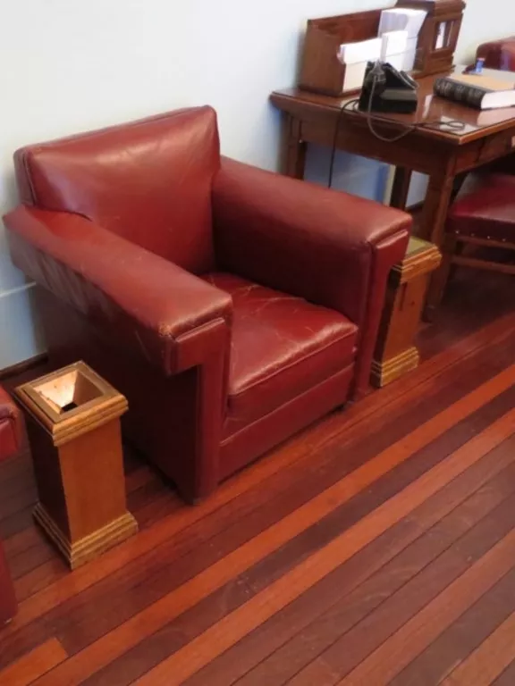 Rectangular wooden pedestal ashtray sitting between two red leather chairs.