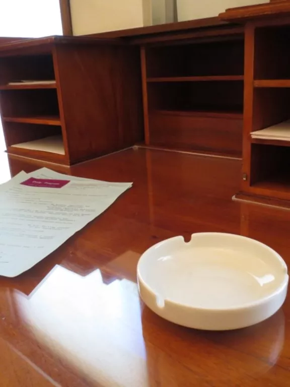 A round white ceramic ashtray sitting on a wooden desk.