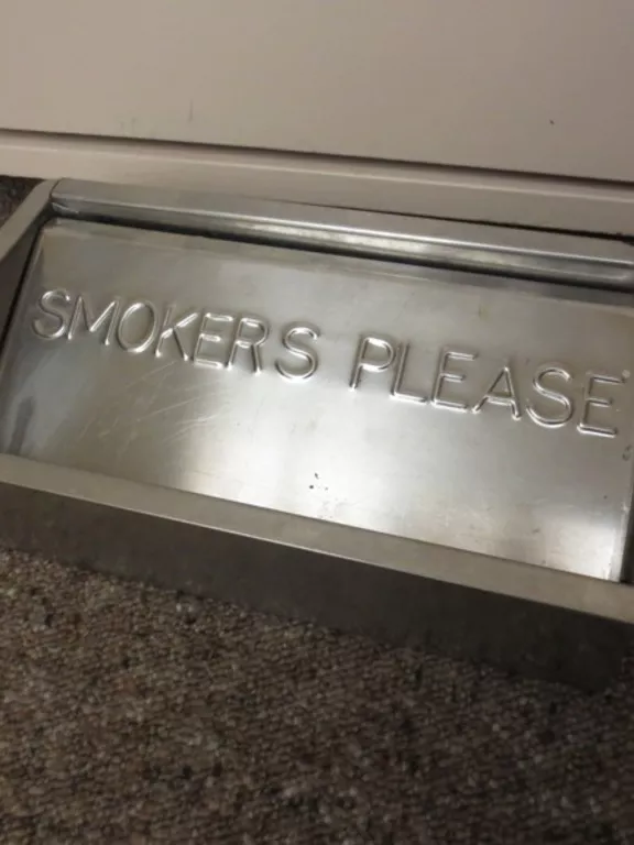 A metal floor ashtray with the inscription 'SMOKERS PLEASE'.