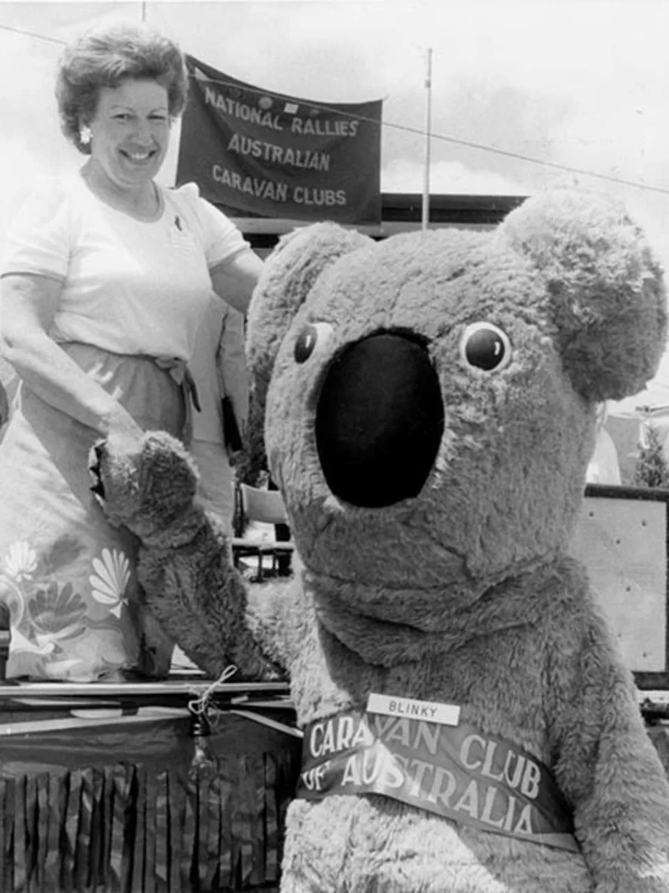 Senator Margaret Reid shakes hands with a person wearing a large koala costume with the nametag 'Blinky'.