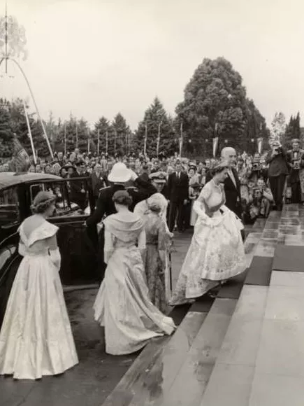 Queen Elizabeth walks up the stairs of Old Parliament House in 1954, wearing a formal gown and surrounded by people. 