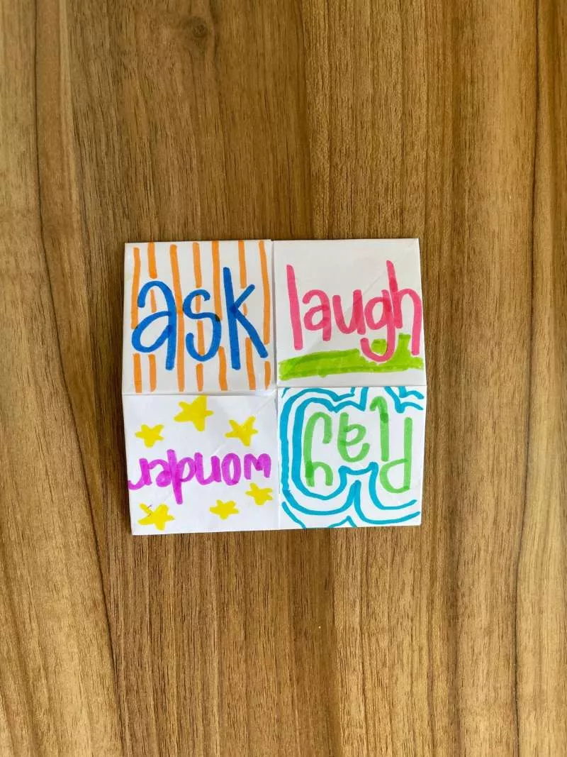 A piece of folded paper with the words ask, laugh, wonder, play.