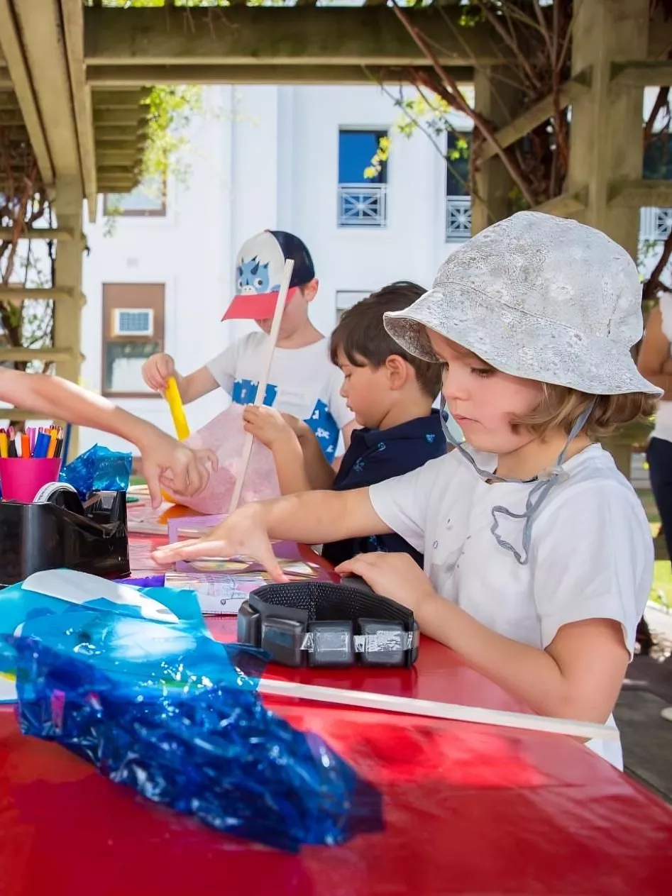 Four children stand around a table outdoors, each focusing on an idividual craft project.