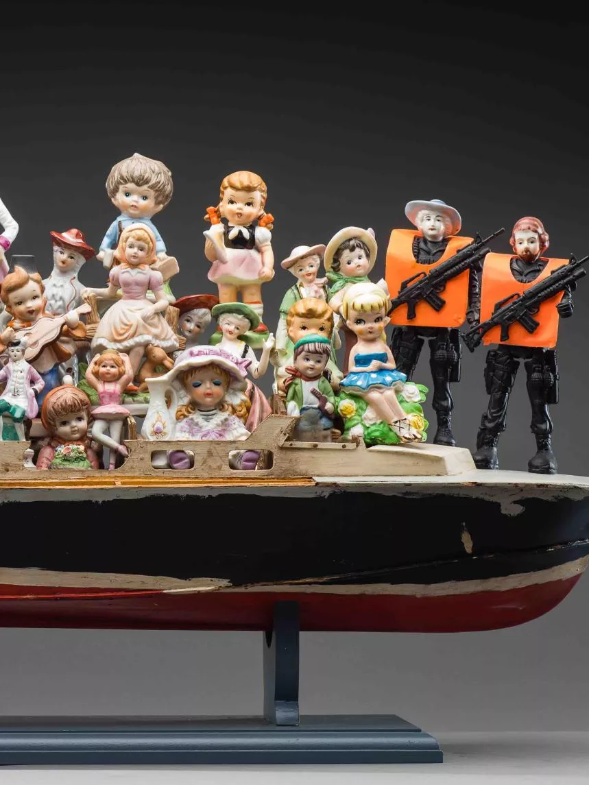 A porcelain statue of a boat filled with men, women and children in formal old fashioned outfits wearing bonnets, waist coats and bows and hats. There are 3 figurines win all black with orange vests and machine guns. 