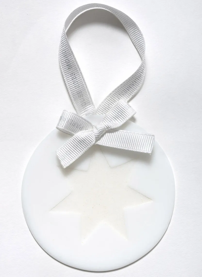 A circular white ornament with a six-pointed start in the centre, with a white ribbon tied in a bow at the top. 