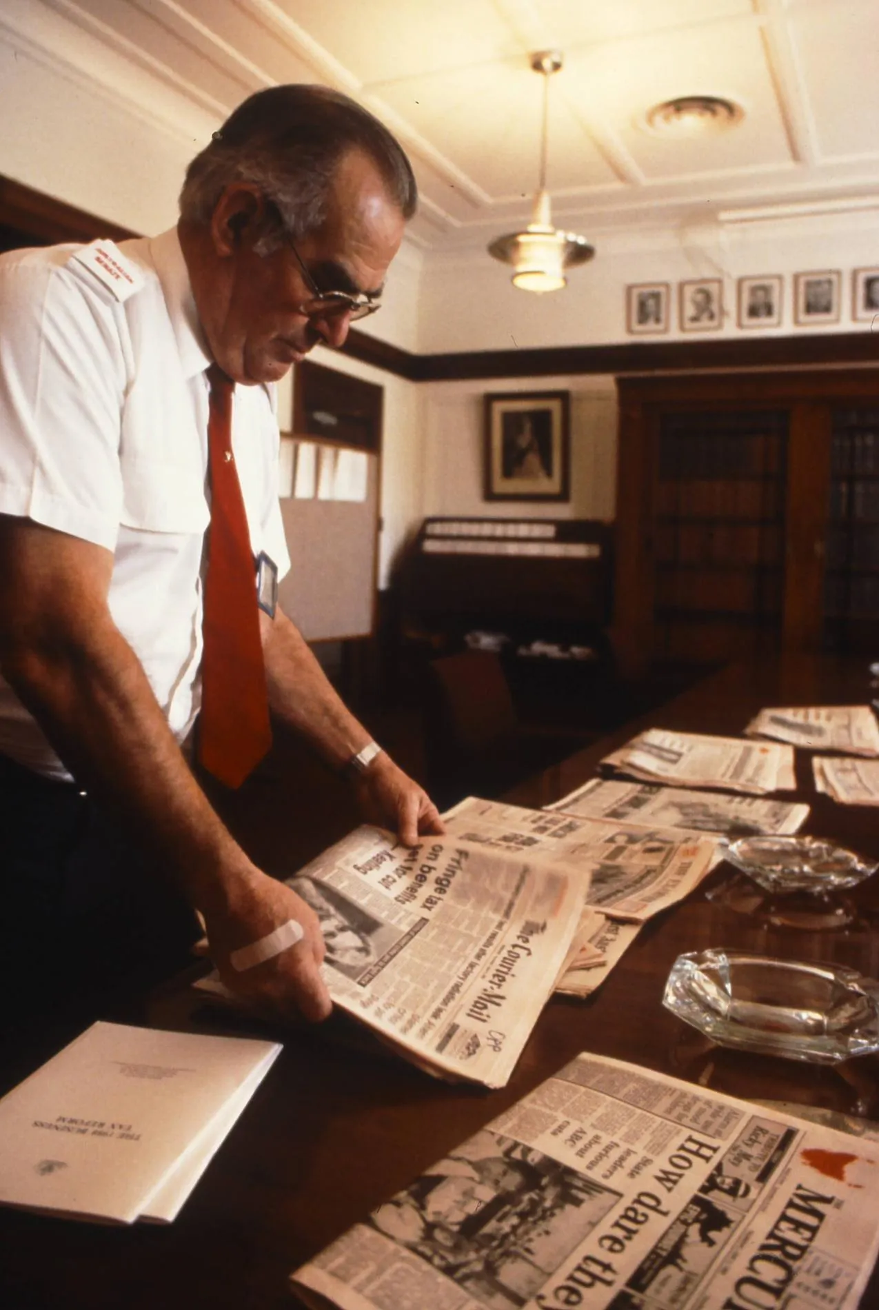 A man wearing a white shirt and red tie arranges newspapers on a table in Old Parliament House.