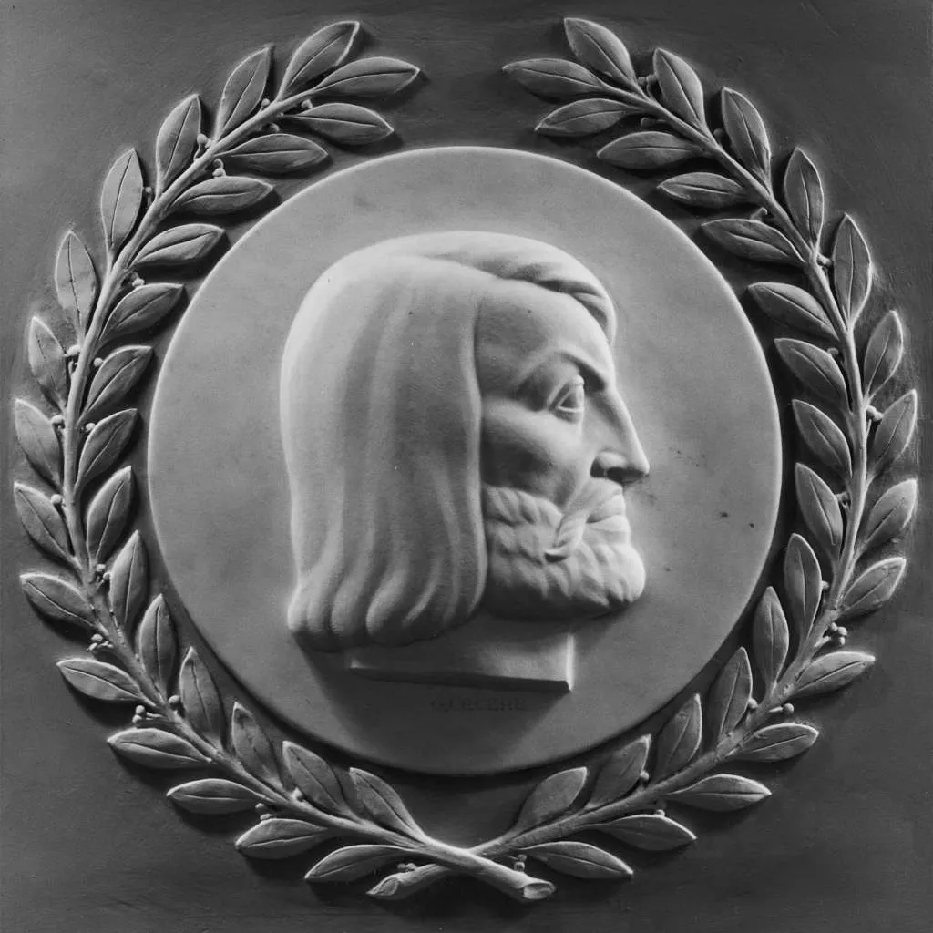 A carved profile of a man's head with long hair and beard, framed with a laurel wreath with the words 'de MONTFORT'.