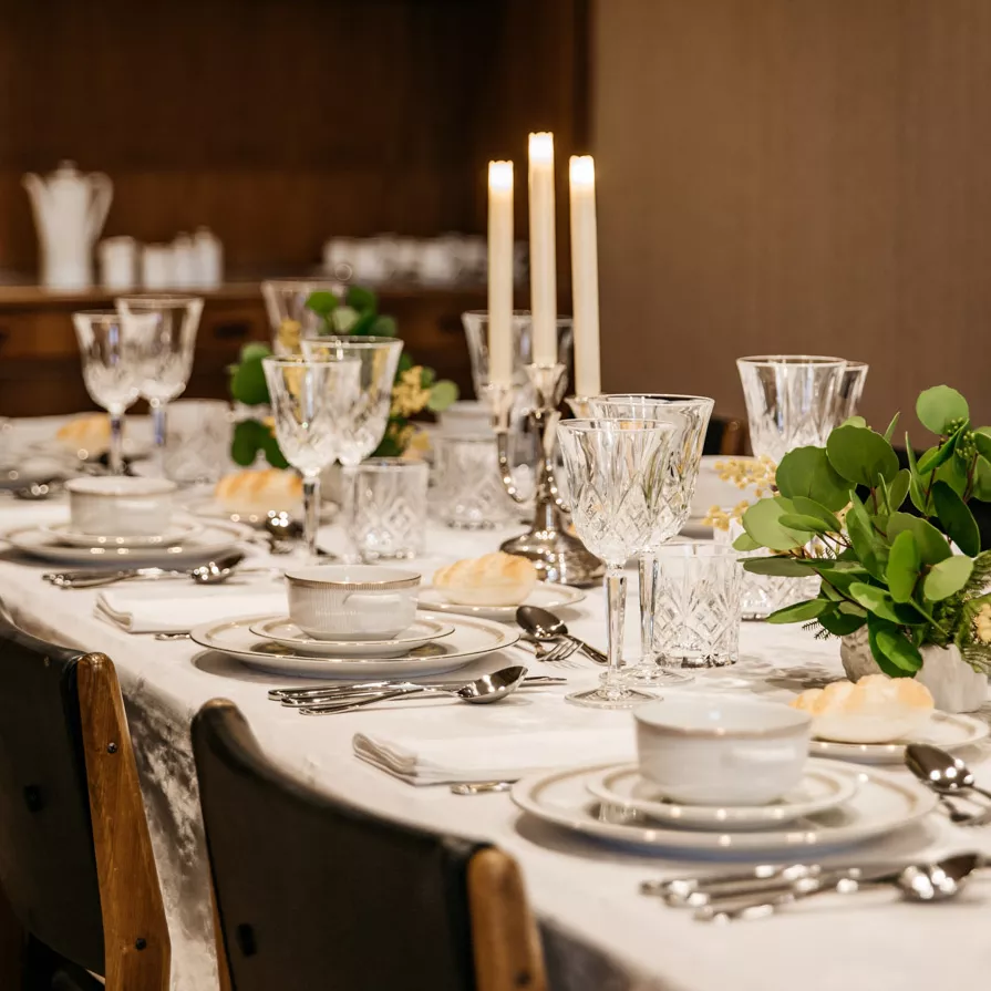 A dinner table set up with china, white linens, silverware and white candles ready for a dinner party