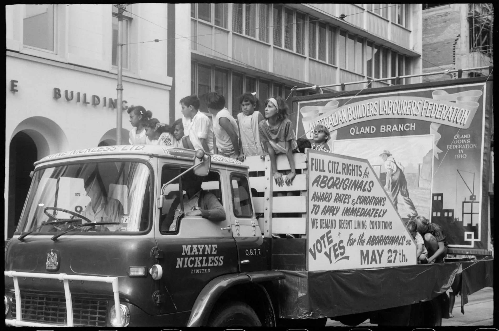 A black and white photo of a car and a float with a group of people standing in front of a sign that reads full citz rights for Aboriginals.