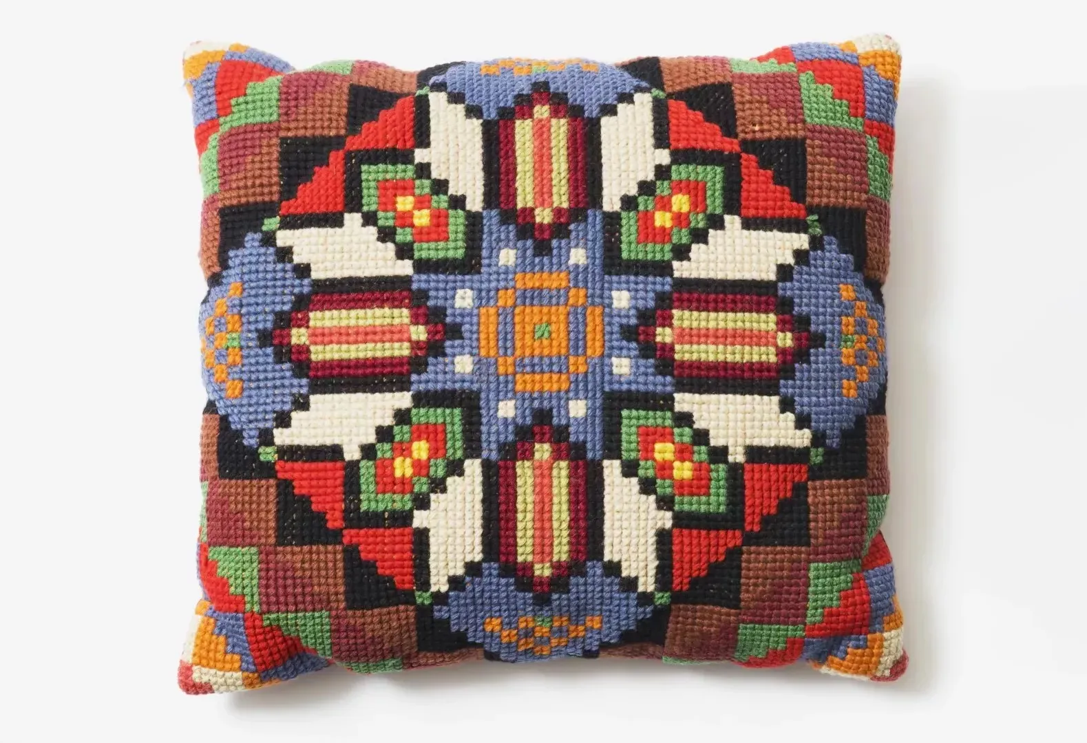 A square embroidered cushion with a geometric pattern using green, yellow, red, blue, orange, black and white threads.