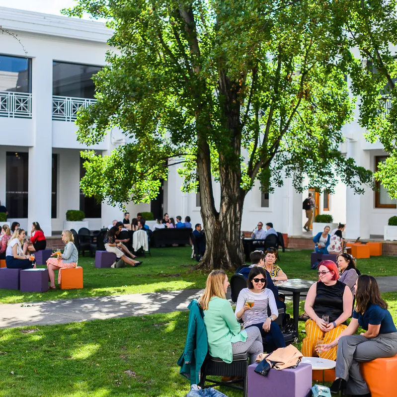 People sit on orange and purple cubes in the courtyard of Old Parliament House having drinks.