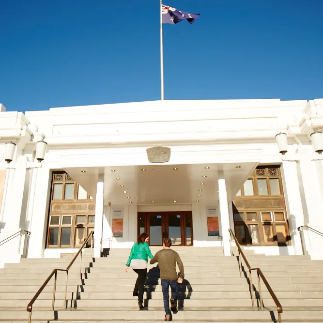 Two people walk up the front entrance steps of Old Parliament House.