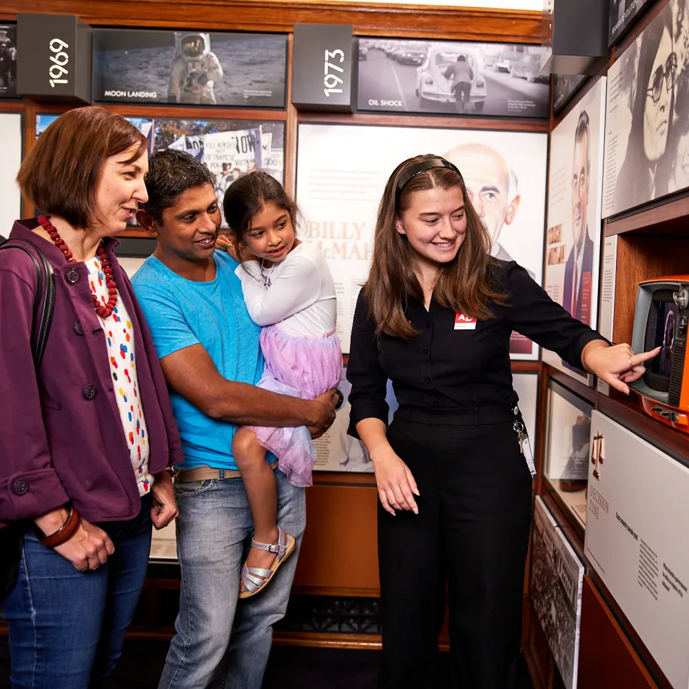 A family and a museum staff member look at an old-fashioned orange television set in an exhibition featuring Australian prime ministers at Old Parliament House.