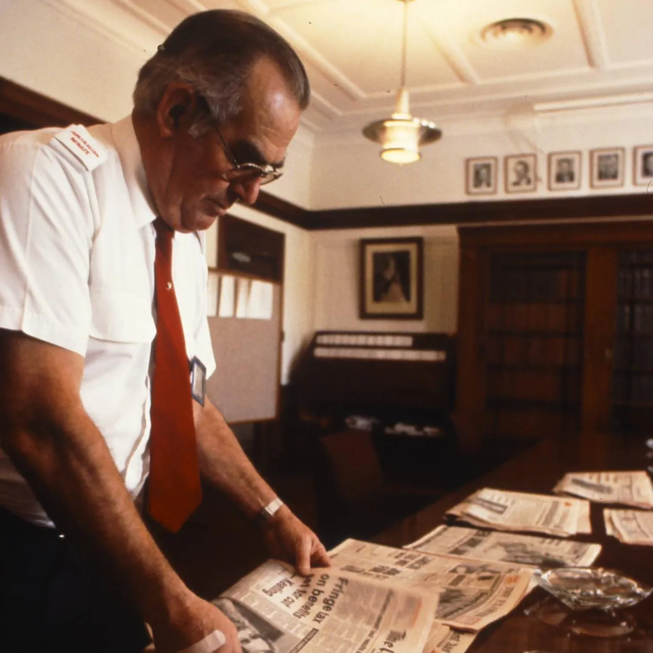 A man wearing a white shirt and red tie arranges newspapers on a table in Old Parliament House.