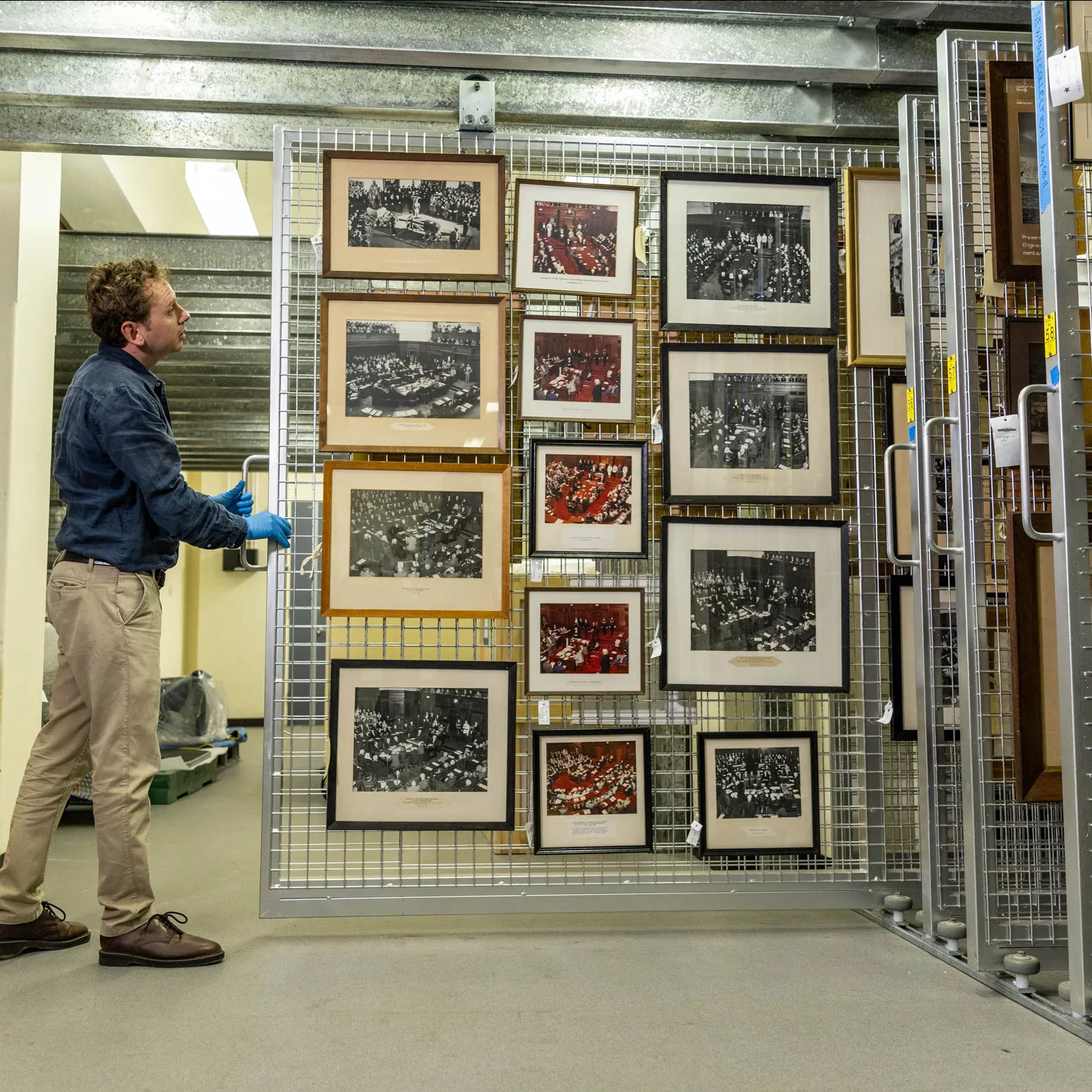 A man pulls a sliding storage display featuring framed pictures in Old Parliament House.
