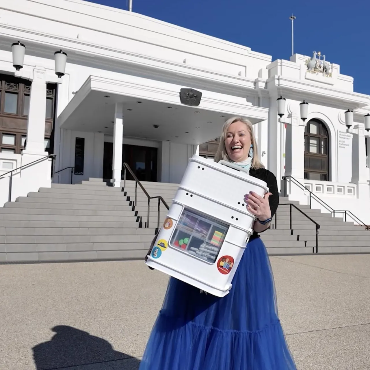 A woman in a blue skirt holds a box of activities outside Old Parliament House. A woman in a blue skirt holds a box of activities outside Old Parliament House.