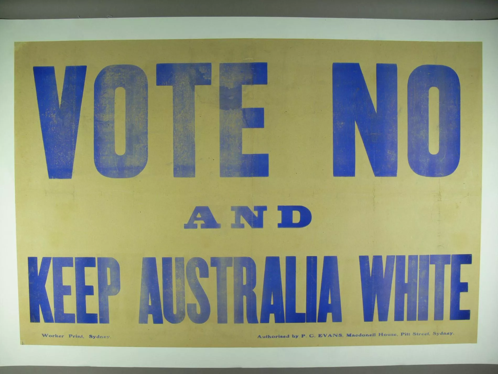 A faded yellow poster with writing in blue capital letters that says ' Vote no and keep Australia white'.