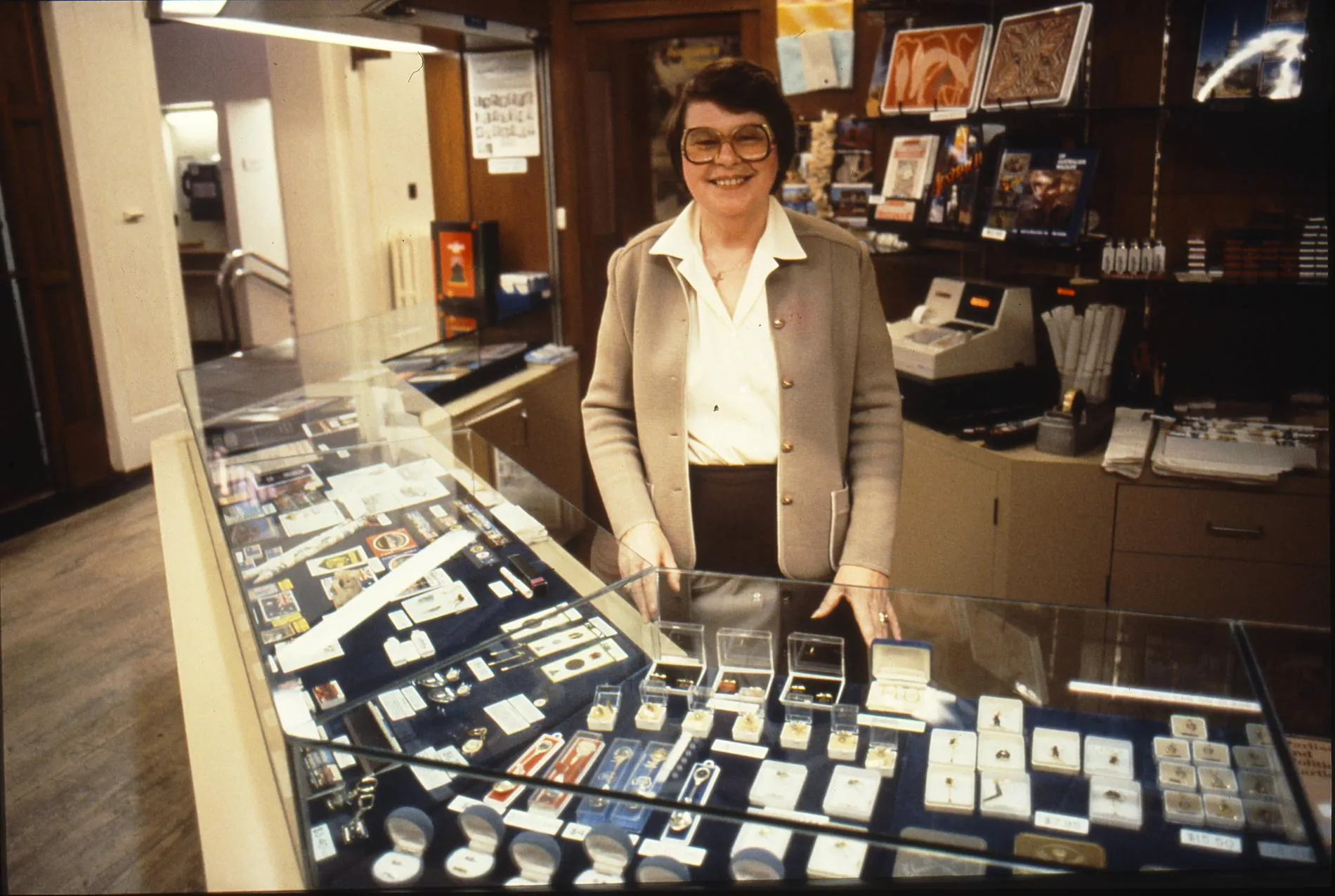 A smiling woman stands behind a glass display cabinet full of souvenirs in the gift shop at Old Parliament House.